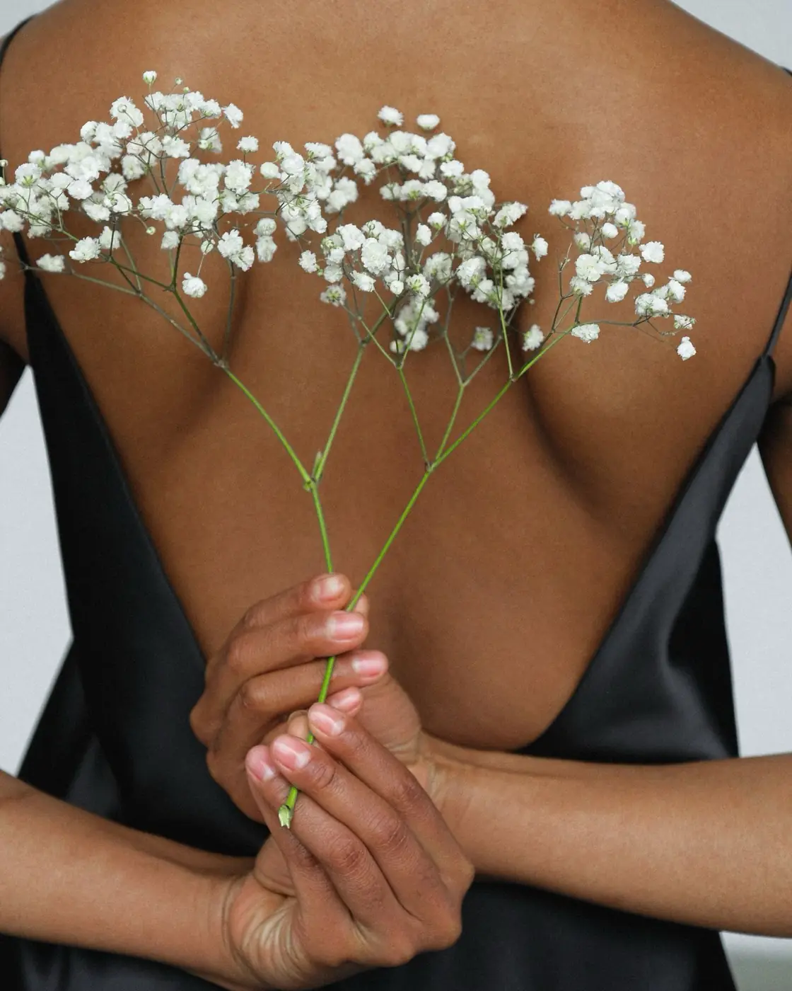 Dos d'une femme tenant une branche de gypsophile blanche — le soin esthétique, jusqu'au bout de la cure